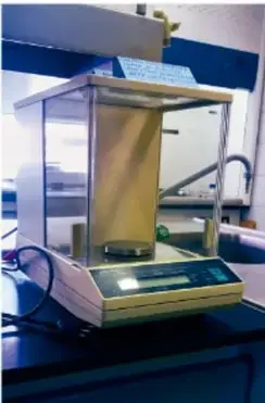 Balanza analítica de precisión (microbalanza) con cámara de vidrio sobre una mesa de laboratorio, empleada para pesar masas muy pequeñas.