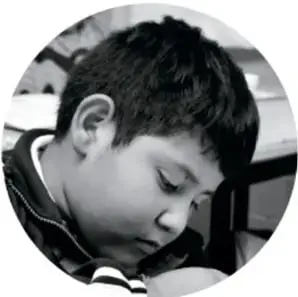Fotografía circular en blanco y negro de un niño inclinado, aparentemente escribiendo o dibujando.