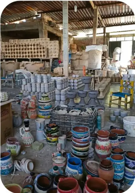 Ilustración de un taller de escultura con varias figuras en yeso, un artesano sentado trabajando y materiales alrededor.