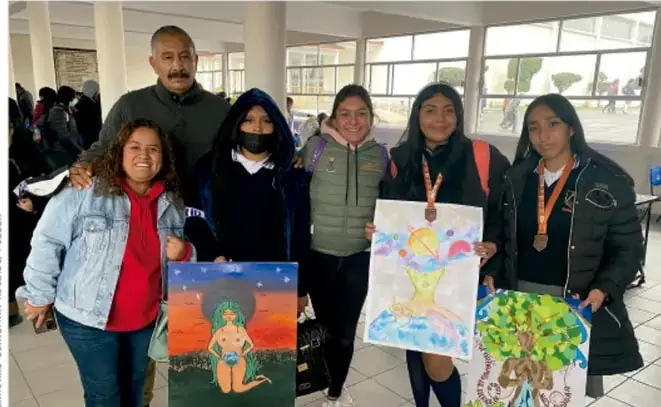 Fotografía de estudiantes y docente sosteniendo pinturas y trabajos realizados en el proyecto, en un espacio escolar abierto. Crédito fotográfico: Gimena Schiaffini Rojas, PIRLA.