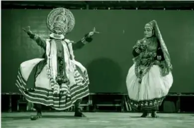 Fotografía a color (en tonos verdes en la reproducción del libro) de dos danzantes de Kathakali en un escenario: el izquierdo con tocado circular multicolor, brazos levantados y piernas abiertas; el derecho con tocado cónico y velo rosa, huipil floreado, brazos cruzados y pies juntos; ambos con maquillajes elaborados.