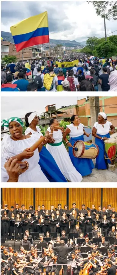 Multitud de personas en una marcha con banderas de Colombia, en un paisaje urbano.