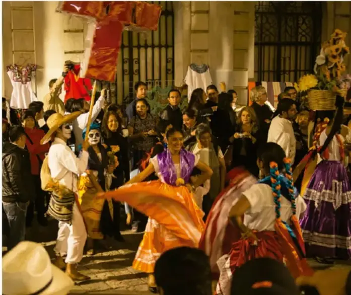Fotografía de una danza tradicional mexicana en una plaza, con participantes con vestimenta colorida, sombreros y máscaras rodeados de espectadores.