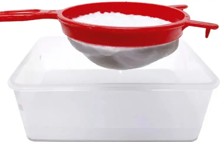 Escurridor rojo con la masa blanca de papel dentro, colocado sobre un recipiente de plástico transparente.