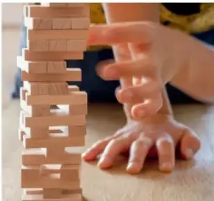 Manos de un estudiante colocando una pieza en una torre de bloques de madera, como metáfora de estrategia y equilibrio.