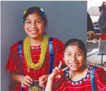 Fotografía de dos niñas indígenas sonrientes con ropa tradicional y collares de cuentas de colores.