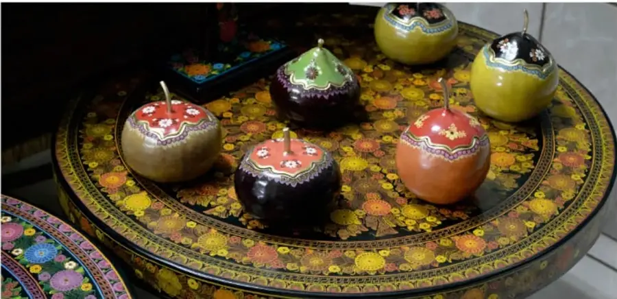 Mesa redonda de madera decorada con motivos florales pintados, sobre la cual se apoyan varias piezas esféricas artesanales (baúles/joyeros) con tapa, de distintos colores y estampados, correspondientes al copalcuahitl y el xochicopal.