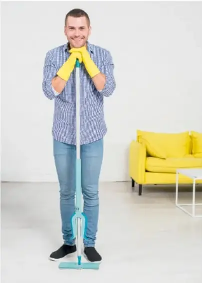 Persona con guantes amarillos sosteniendo un trapeador, en una sala con sillón amarillo.