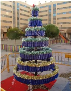 Árbol navideño elaborado con botellas plásticas y ecoladrillos, colocado en el patio de una escuela.