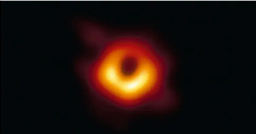 Imagen de un agujero negro con un anillo luminoso naranja y amarillo alrededor de una zona central oscura.