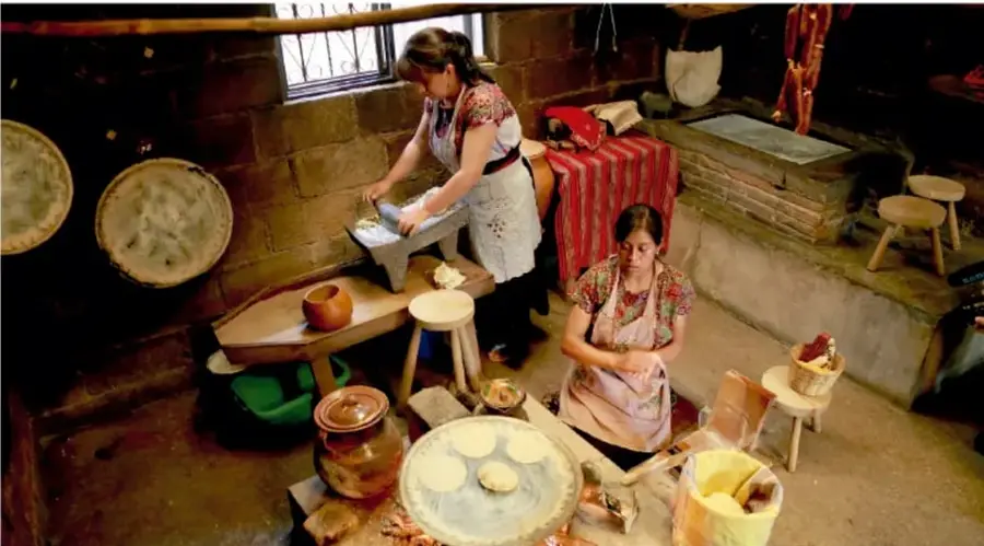 Dos mujeres elaborando tortillas y alfarería en un taller con utensilios de barro.