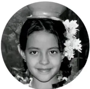 Fotografía en blanco y negro de una niña sonriente con flores blancas en el cabello.