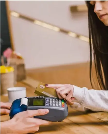 Fotografía de una persona pagando con tarjeta en una terminal de punto de venta (datáfono), ilustrando la transacción comercial y el precio de venta.
