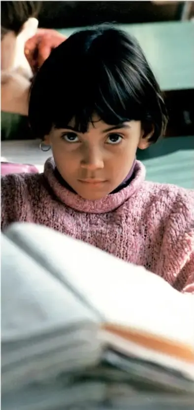 Fotografía de una niña leyendo un libro, con suéter rosa.
