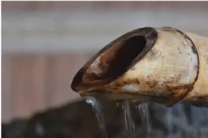 Fotografía de un tubo de bambú cortado en diagonal que escupe un chorro de agua; se ve claramente que está hueco por dentro.