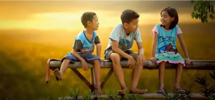 Fotografía de tres niños sentados sobre una valla de madera al atardecer, conversando y sonriendo, en un paisaje natural.