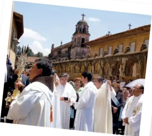 Procesión religiosa con personas vestidas de blanco y una iglesia al fondo.