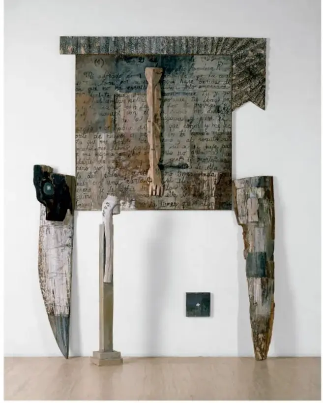 Fotografía de la instalación 'Formas violadas' (1994) de Alejandro Aguilera. Se observa un panel rectangular con escritura manuscrita y una figura humana incompleta, acompañado de dos piezas alargadas de madera o material orgánico a los lados y una pequeña base central. La obra está montada sobre una pared blanca en una sala de museo.