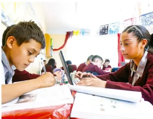 Fotografía de estudiantes trabajando con laptop y materiales en el aula.