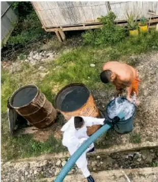 Fotografía de una comunidad rural donde varias personas trabajan juntas alrededor de tambos y una manguera, posiblemente en labores de abastecimiento de agua o limpieza, lo que ilustra el trabajo comunitario.