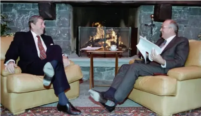 Fotografía de dos hombres sentados en sillones frente a una chimenea conversando (cumbre de líderes de EE. UU. y la URSS, probablemente Reagan y Gorbachov), referencia visual de la Guerra Fría.