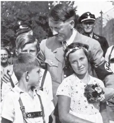 Fotografía en blanco y negro de Adolf Hitler rodeado de jóvenes y una mujer, en un acto público.