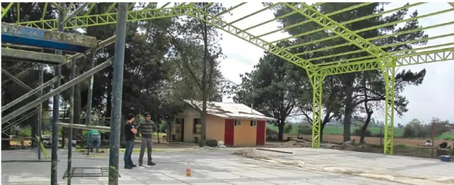 Estructura metálica verde de un patio escolar con estudiantes y edificios al fondo, ilustrando el espacio para montar la exposición.