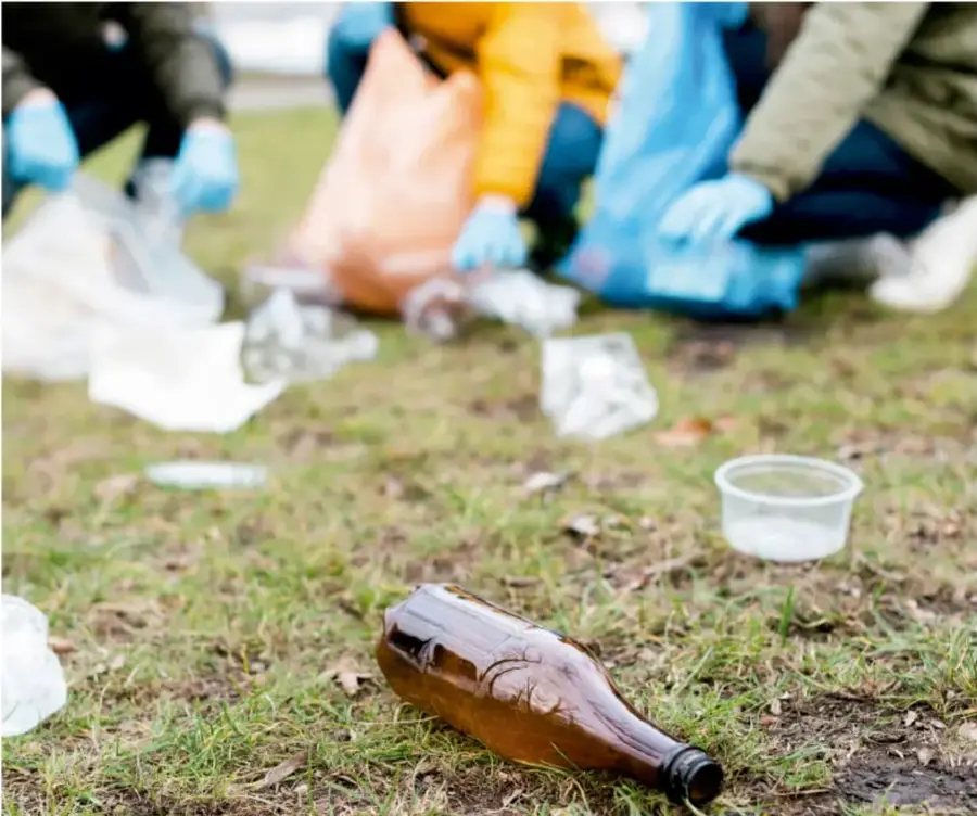 Fotografía de varias personas con guantes recogiendo residuos como botellas de vidrio y envases plásticos en un área verde, ejemplo de acción sostenible comunitaria.
