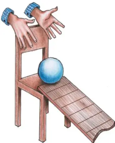 Manos de un niño sobre una tabla apoyada en una silla formando una rampa, con una pelota azul en lo alto de la tabla.