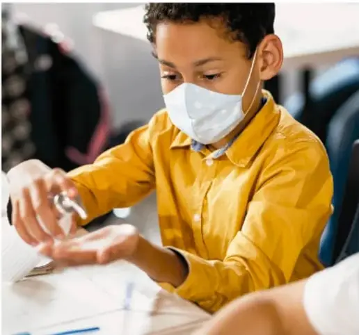 Fotografía de un niño con mascarilla aplicándose gel antibacterial en las manos, ejemplificando higiene y autocuidado físico.