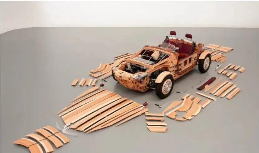 Prototipo de automóvil de madera mostrado junto con todas sus piezas de carrocería desarmadas sobre un piso gris.