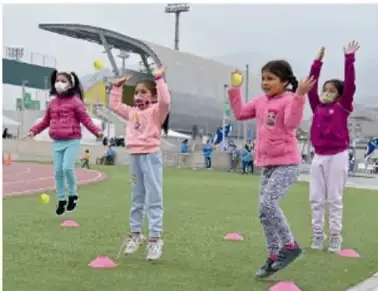 Cuatro niñas en una pista atlética con conos, realizando actividad física.