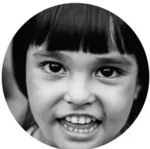 Fotografía en círculo de una niña sonriente de cabello negro con flequillo, junto a la adivinanza.