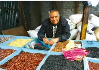 Persona sentada vendiendo granos y semillas en un mercado local.