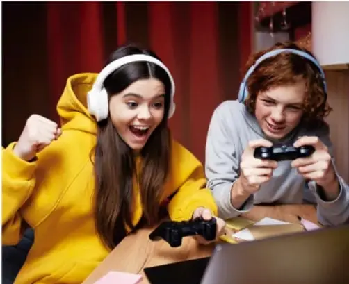 Dos adolescentes con audífonos jugando videojuegos frente a una pantalla, ejemplo de sedentarismo.