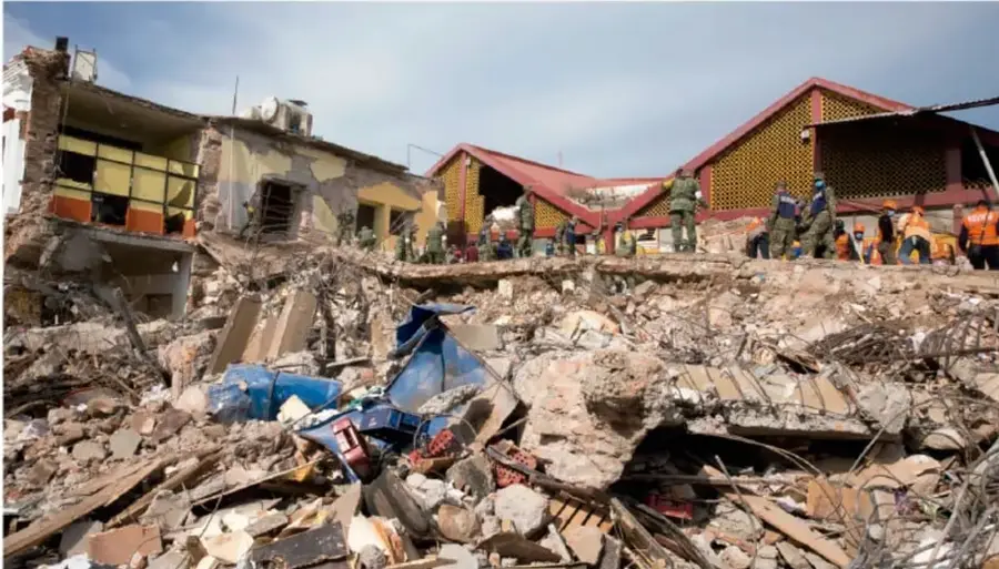 Fotografía de una zona urbana devastada por un sismo, con edificios colapsados, escombros y personal de rescate trabajando entre los restos.