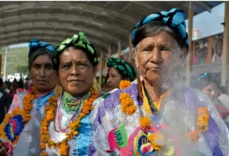 Mujeres indígenas con vestimenta tradicional y guirnaldas de flores, representando pautas de convivencia de cultura ancestral.