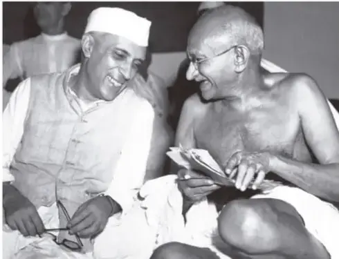 Fotografía en blanco y negro de Mahatma Gandhi y Jawaharlal Nehru conversando y revisando documentos.