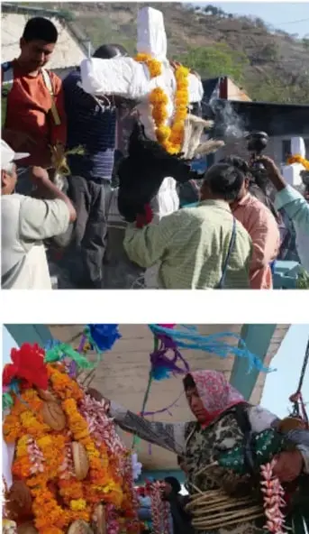 Personas cargando una figura religiosa adornada con flores durante una procesión en una comunidad indígena.