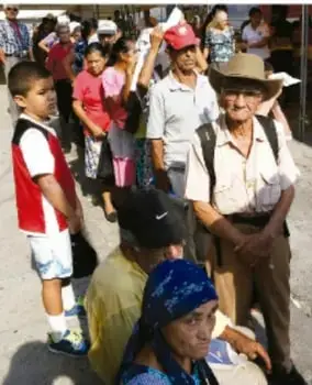 Fotografía de personas en una calle, entre ellas un adulto mayor con sombrero y niños, representando la vida comunitaria.