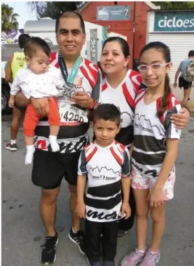Familia (padre, madre y tres hijos) con medallas y camisetas deportivas después de una carrera o evento deportivo.