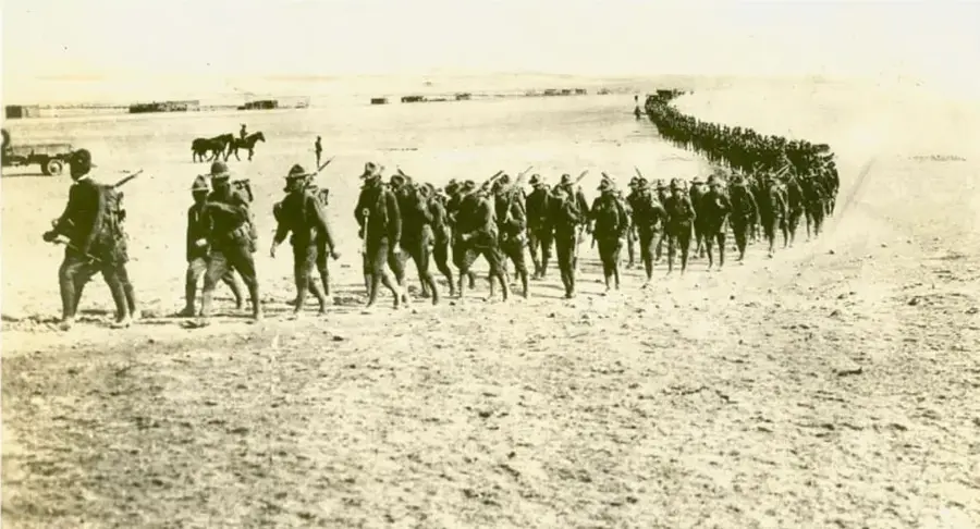 Fotografía histórica en blanco y negro que muestra una columna de soldados revolucionarios marchando en formación por un terreno árido, con algunos jinetes al fondo.