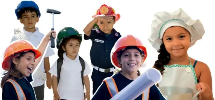 Fotografía de seis niños de primaria disfrazados de distintos oficios: uno con casco y martillo (albañil), una niña con casco naranja y chaleco reflectante (obrera), una niña con casco verde y mochila, un niño con casco de bombero, una niña cocinera con delantal y gorro, y un niño con casco y rollo de plano (arquitecto).