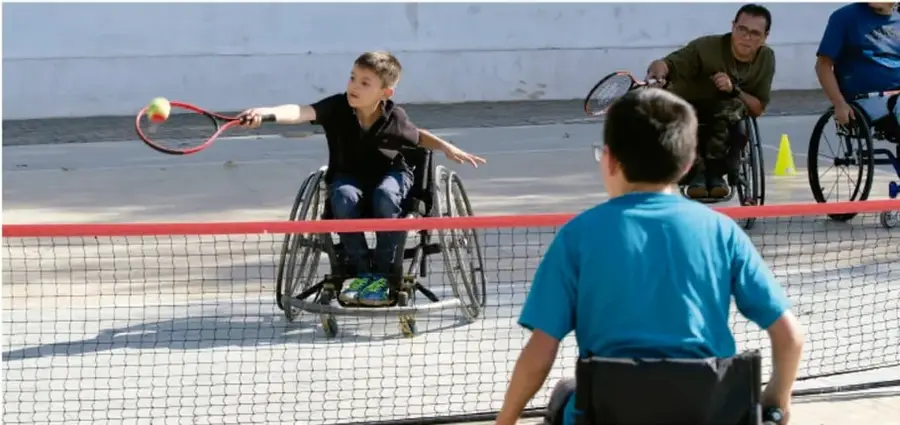 Fotografía de adolescentes jugando tenis en sillas de ruedas sobre una cancha, ilustrando la inclusión deportiva y la participación de personas con discapacidad en actividades recreativas.