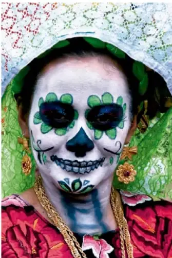 Fotografía de una persona con el rostro pintado como calavera (Catrina) con maquillaje verde y flores, tradición del Día de Muertos.