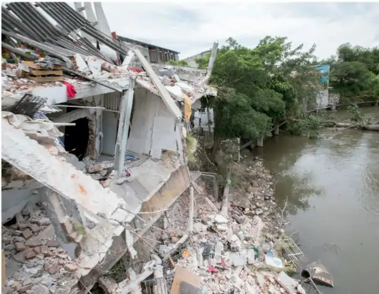 Fotografía de un edificio colapsado tras un sismo, con escombros y estructuras de concreto derrumbadas junto a un río.