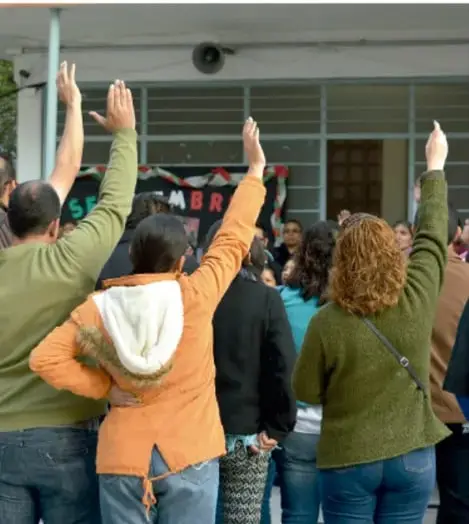 Fotografía de un grupo de estudiantes levantando las manos durante una asamblea o actividad escolar de convivencia.