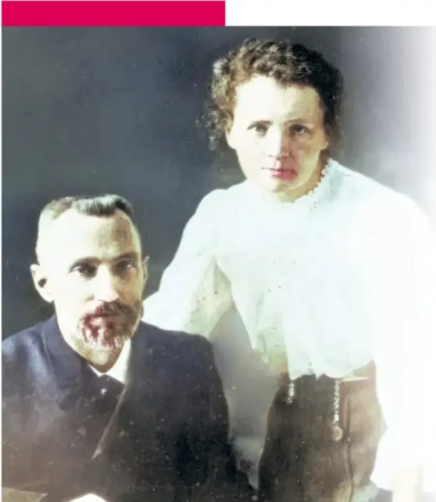 Fotografía antigua coloreada de Marie Curie de pie junto a un mueble de madera, con vestido negro largo de la época, en su primer tiempo en París.