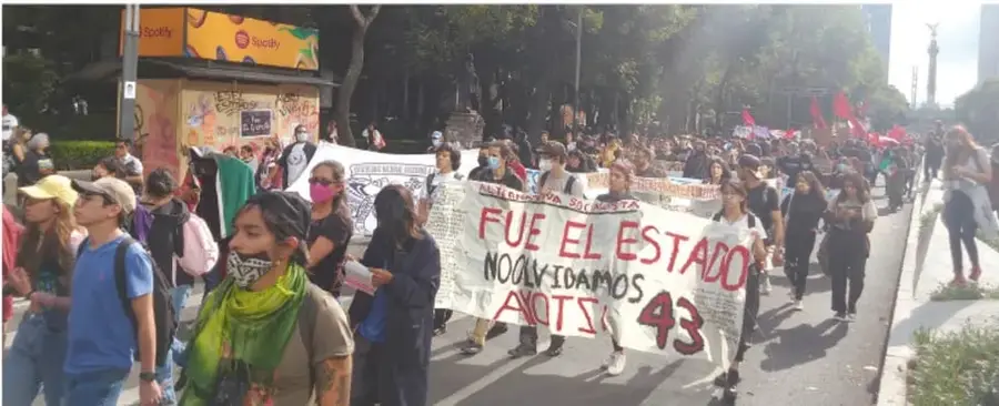 Fotografía de una marcha con personas sosteniendo una pancarta que dice 'FUE EL ESTADO' y 'NO AYOTZINAPA 43'.