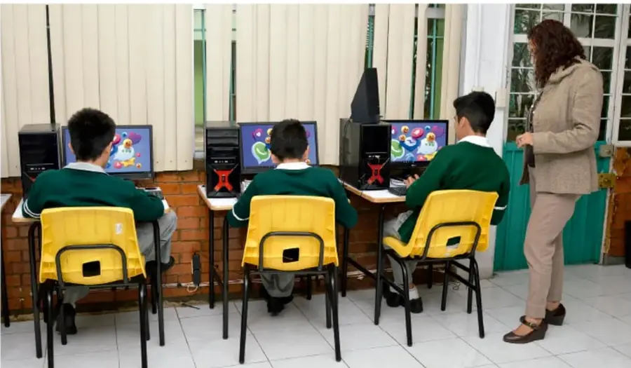 Fotografía de estudiantes de secundaria usando computadoras en un aula con su maestra supervisando.